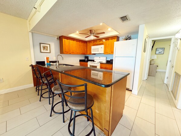 A kitchen with wooden cabinets, a central island with bar stools, a ceiling fan, and a microwave.