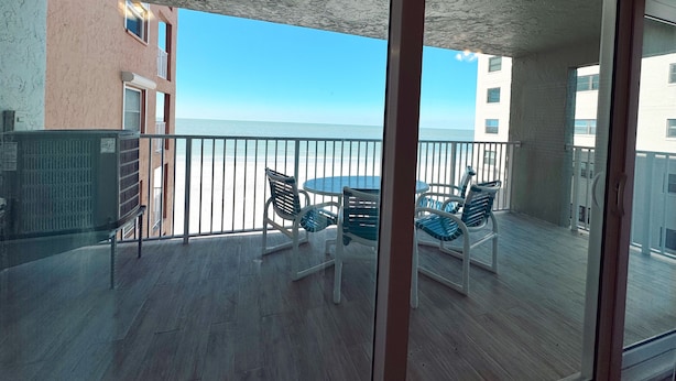 A balcony with a table and chairs, overlooking a beach.