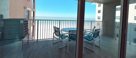 A balcony with a table and chairs, overlooking a beach.