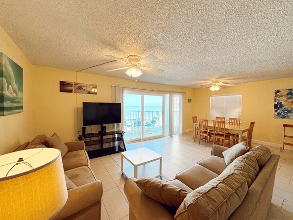 A spacious living room with a large flat-screen TV, a ceiling fan, and a dining area with a table and chairs.