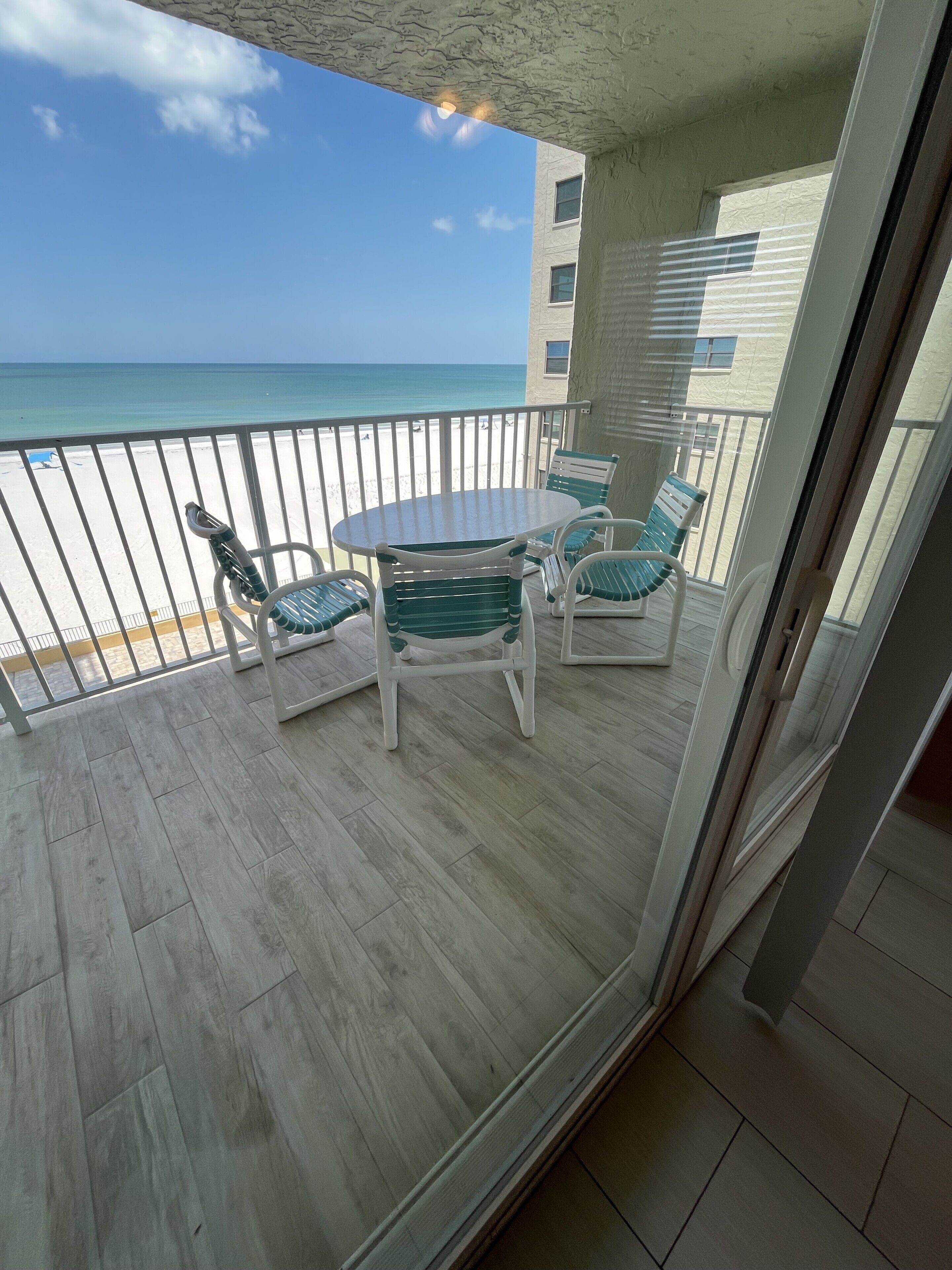 A balcony with a table and chairs, overlooking a beach and ocean.