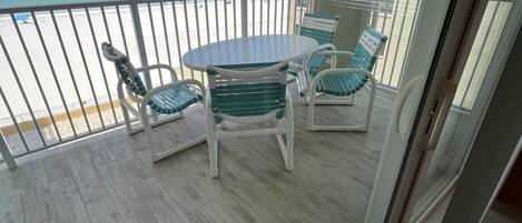 A balcony with a table and chairs, overlooking a beach and ocean.