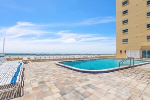 A rooftop swimming pool with lounge chairs, a clear view of the ocean, and a building with multiple windows.