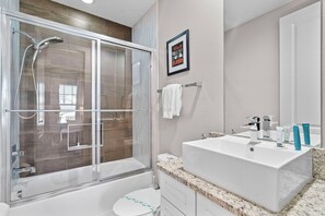 Une salle de bain moderne avec une douche à parois de verre, un lavabo blanc et une citation inspirante encadrée au mur.