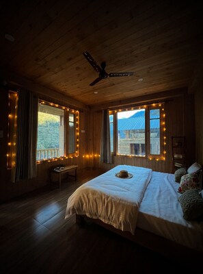 Une pièce chaleureuse en bois, avec un lit, un ventilateur de plafond et des fenêtres décorées de guirlandes lumineuses.
