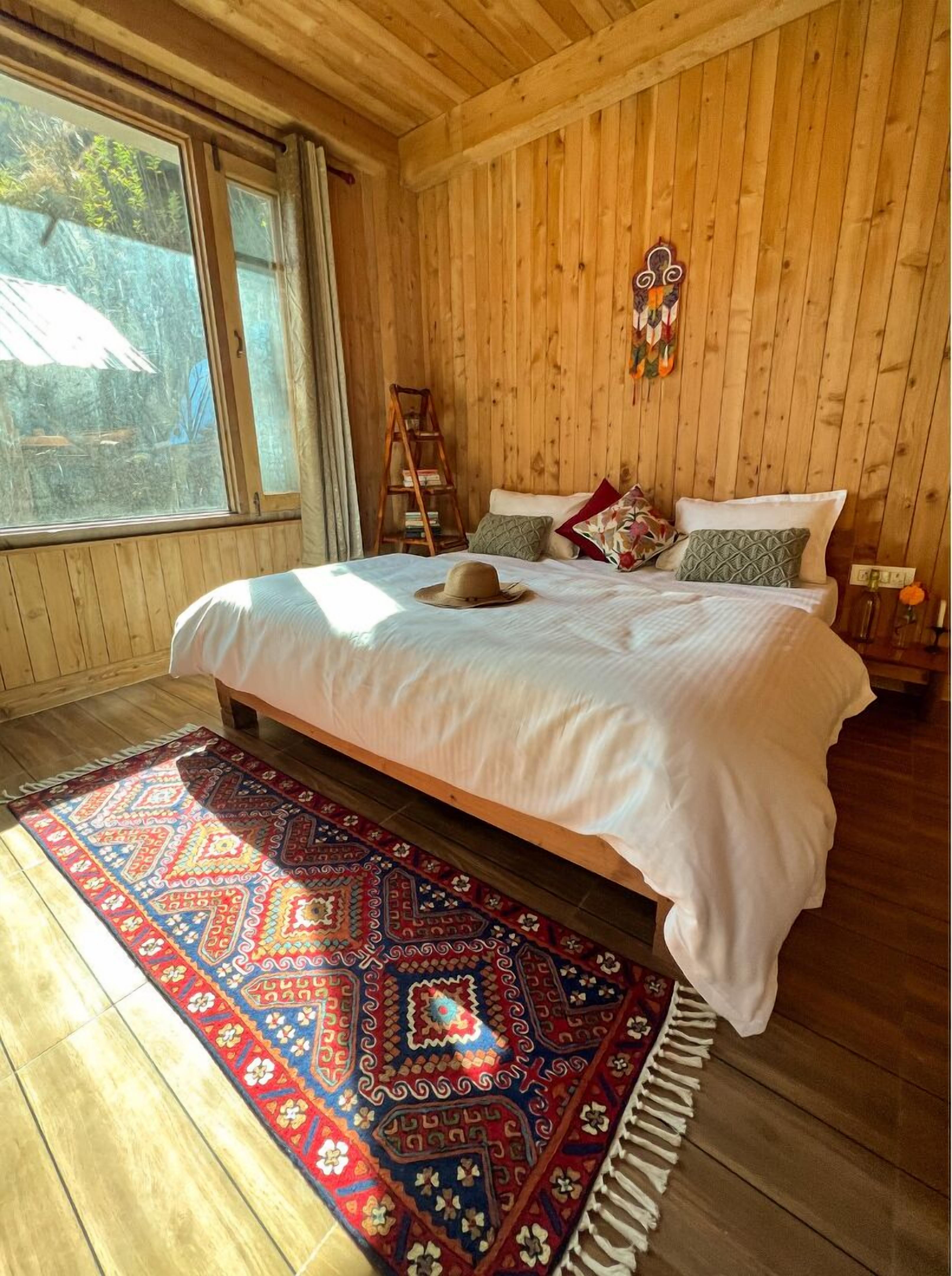 A wooden-paneled bedroom with a bed, a colorful rug, and a ladder against the wall.