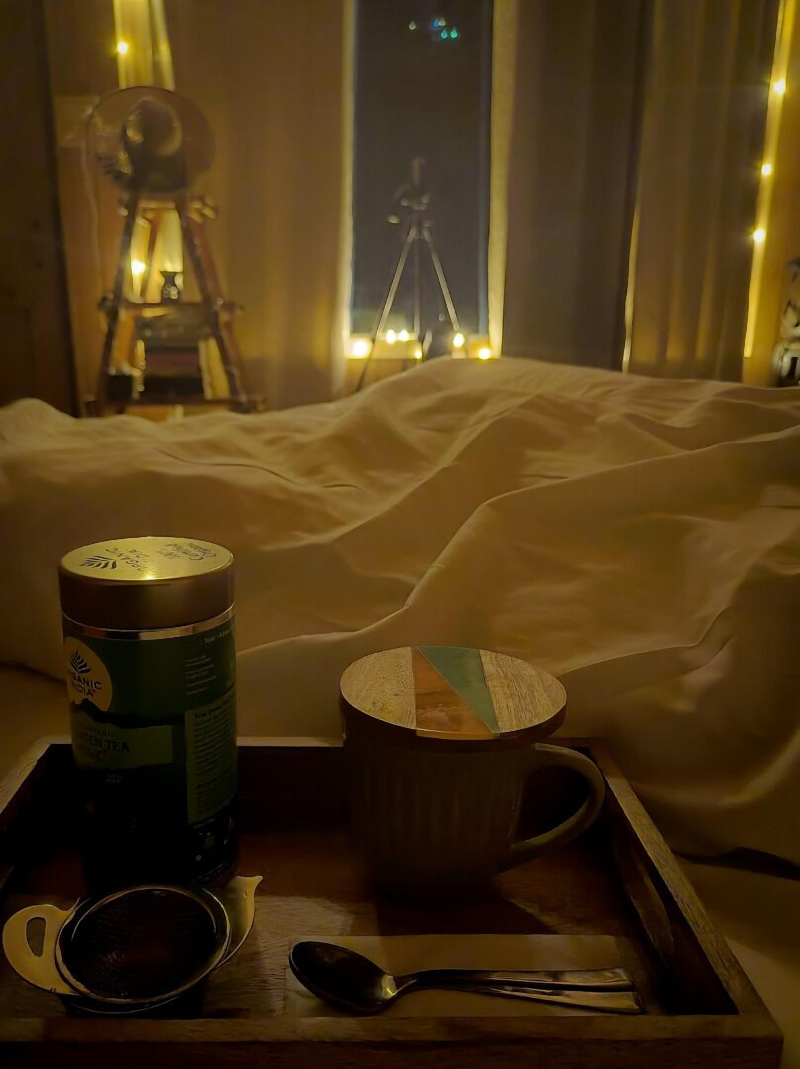 Ein gemütliches Zimmer mit einem Bett, einem Tablett mit einer Teedose, einer Tasse, einem Löffel und einer Kamera auf einem Stativ.