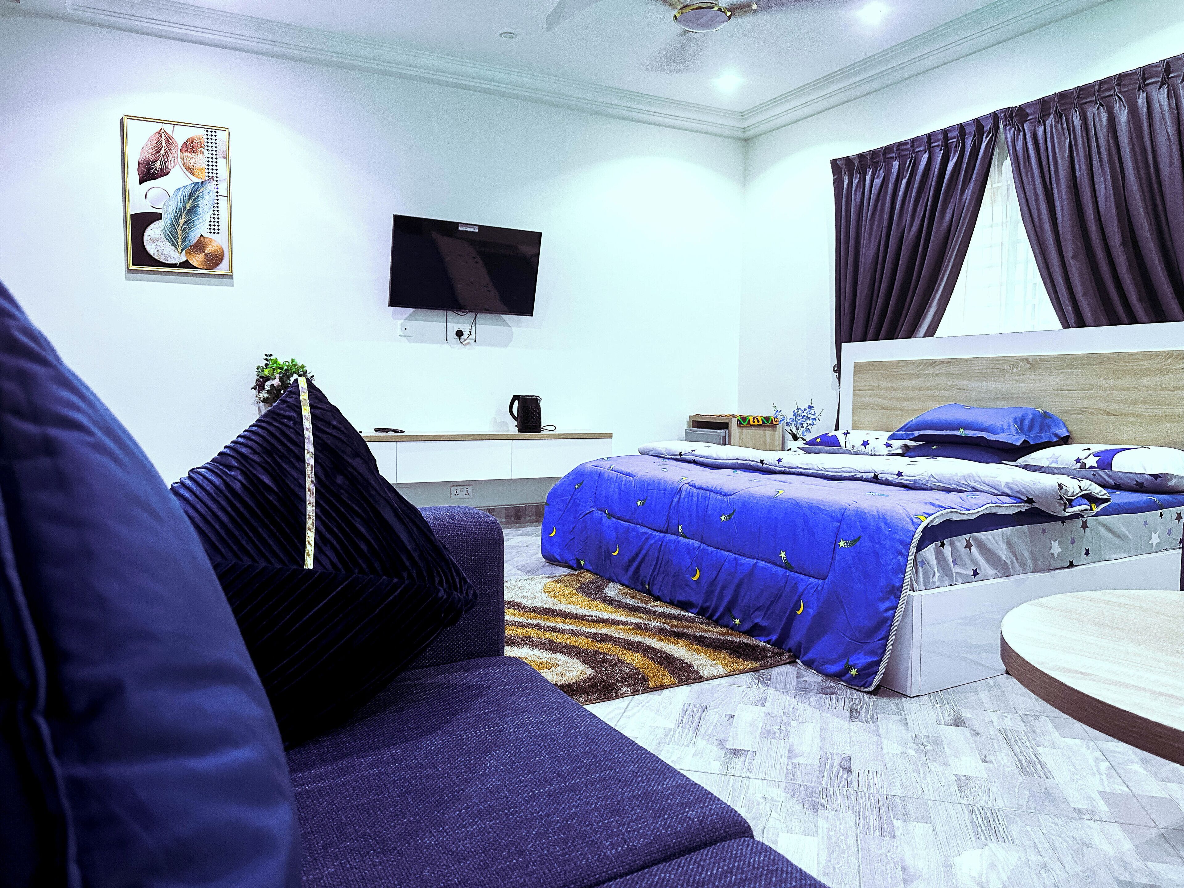 A modern bedroom with a bed, a sofa, a TV, and a window with curtains.
