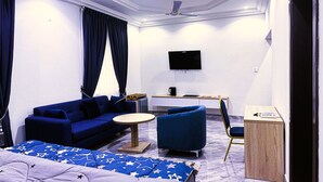 A modern hotel room with a blue sofa, a round coffee table, a bed with a star-patterned duvet, a desk with a flat-screen TV, and a chair. - Firnic Luxurious Private Hotel (Kwabenya)