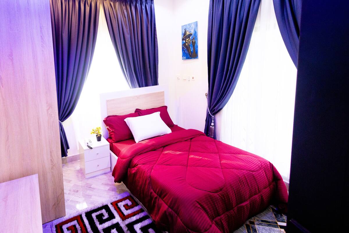 A bedroom with a bed, curtains, a ceiling fan, and a painting on the wall.