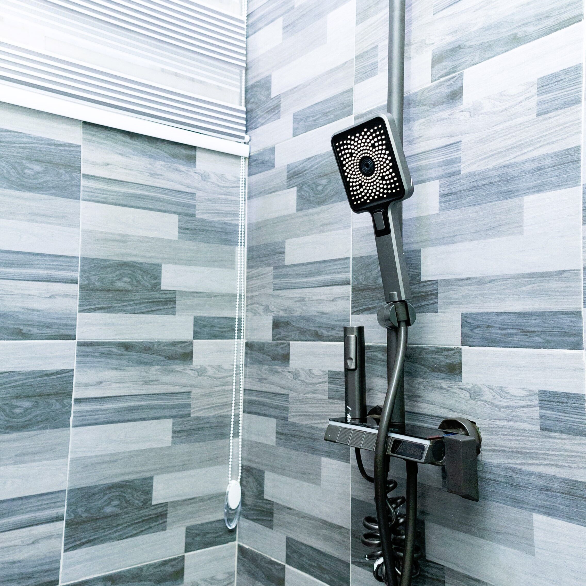 Une douche équipée d’un pommeau de douche à main fixé au mur, d’un panneau de commande et d’un flexible.