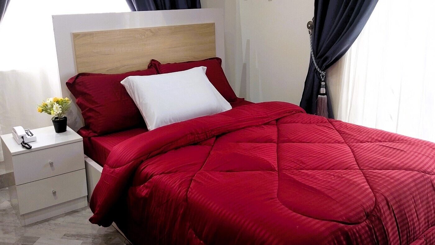 Una cama con colcha roja, almohada blanca y cabecera de madera.