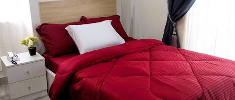 Una cama con colcha roja, almohada blanca y cabecera de madera.