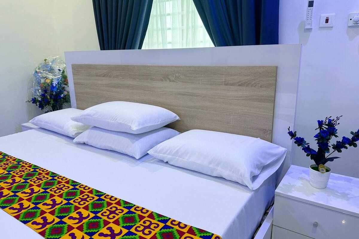 A neatly made bed with white bedding and a colorful geometric-patterned blanket.
