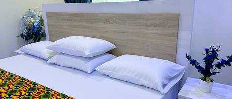 Una cama bien hecha con ropa blanca y una manta de diseño geométrico y colores vivos.