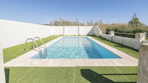 A rectangular swimming pool with a metal ladder, surrounded by a concrete wall and a grassy area.