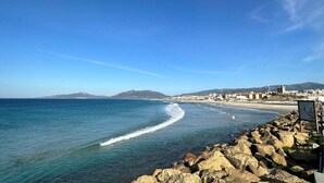 A coastal view with a rocky shoreline, a clear blue sky, and distant buildings.