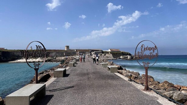 A coastal walkway with metal signs reading "Mar Mediterraneo Tarifa" and "Océano Atlántico Tarifa".