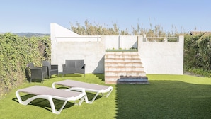 A modern outdoor patio with two lounge chairs, a small table, and a concrete staircase leading to a higher level.