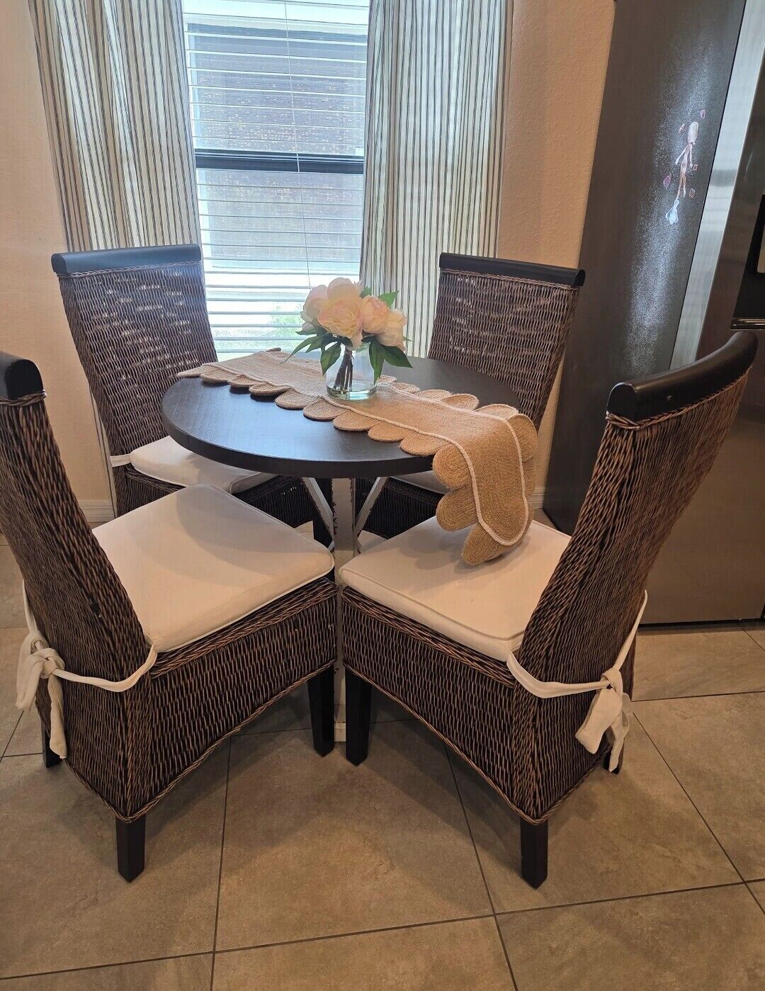 A dining area with wicker chairs, a round table, and a vase with flowers.