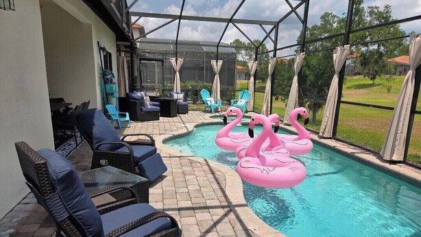 A covered outdoor pool area with lounge chairs, a table, and two pink flamingo floats.
