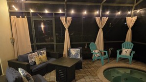 An outdoor patio area with a pool, seating arrangements, and string lights.