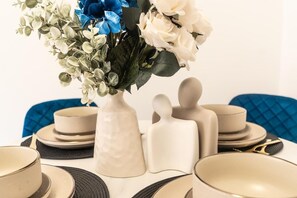 A table set with beige plates, a vase with white and blue flowers, and a white ceramic object.