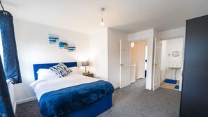 A bedroom with a bed, a nightstand, a lamp, and a door leading to a bathroom. - Collingwood Lodge, Birmingham with FREE Parking (West Midlands)