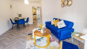 A living room with a blue sofa, a coffee table, and a dining area with blue chairs. - Collingwood Lodge, Birmingham with FREE Parking (West Midlands)