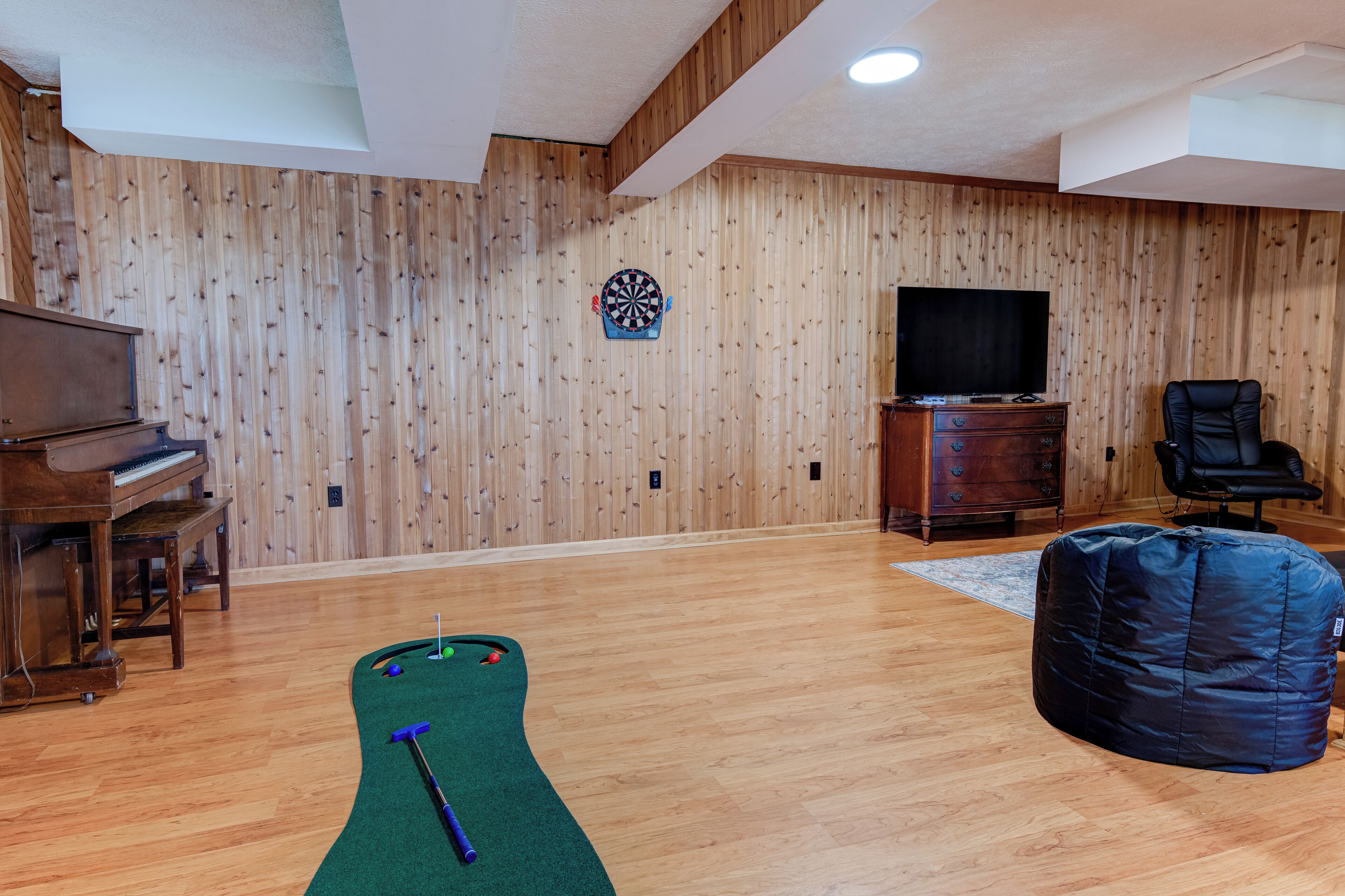 Une pièce avec un mur en bois, un jeu de fléchettes, un téléviseur, un piano, un fauteuil poire et une table de billard.