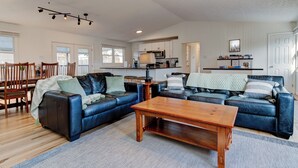 A spacious living room with a large blue leather sofa, a wooden coffee table, and a dining area with wooden chairs and a table.