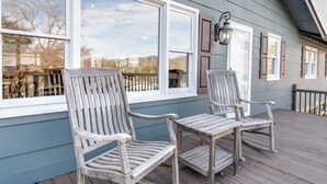 A wooden deck with two rocking chairs and a table, overlooking a fenced area.
