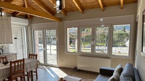 Un vaste espace de vie doté d’un plafond en bois, d’un canapé, d’une table à manger avec des chaises et de grandes fenêtres offrant une vue sur l’extérieur.