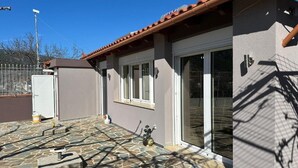 Une maison avec un patio carrelé, une porte-fenêtre coulissante et un petit abri de jardin.