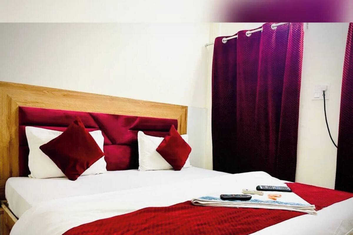 Une chambre d’hôtel avec une tête de lit en bois, du linge de lit blanc, des oreillers rouges et une couverture rouge.