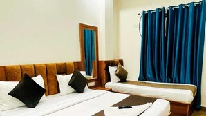 Una habitació d'hotel amb un llit gran, un altre més petit, un mirall i una finestra amb cortines blaves.