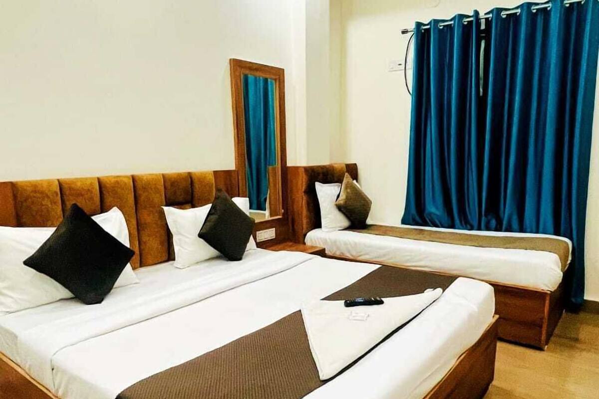 Une chambre d’hôtel avec un grand lit, un plus petit lit, un miroir et une fenêtre avec des rideaux bleus.