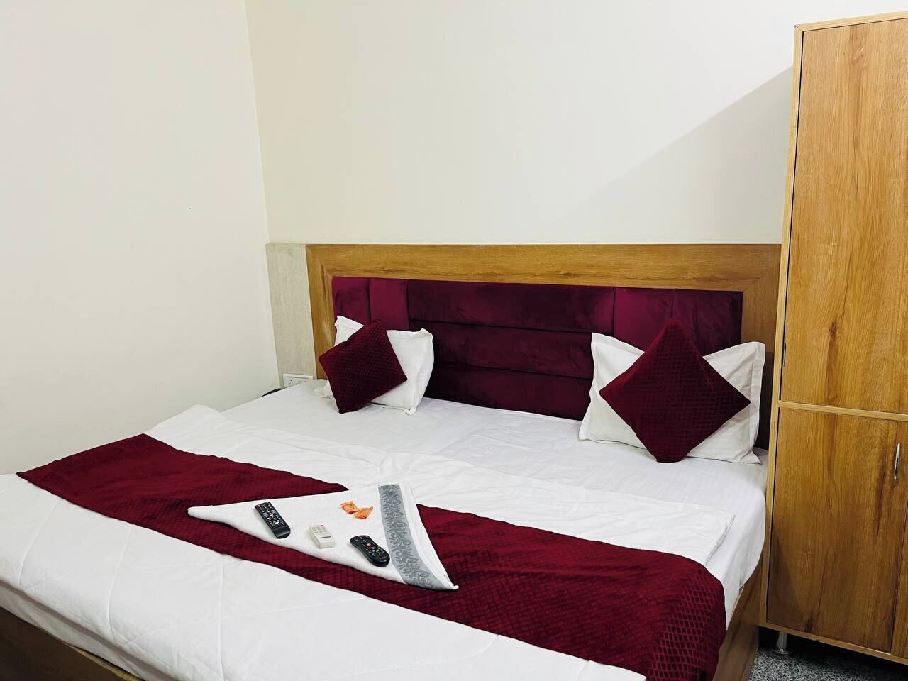 A neatly made bed with a wooden headboard, white bedding, and a red throw blanket.