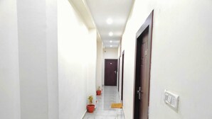 Passadís amb parets blanques, un paviment de marbre i portes a ambdós costats. Hi ha plantes en testos i un interruptor de llum a la paret.