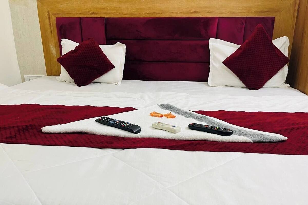 Un lit bien fait, avec une couverture rouge, deux oreillers et une télécommande posée sur le couvre-lit.