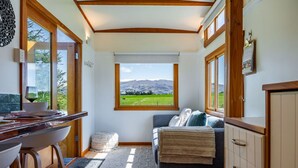 A cozy room with a large window offering a scenic mountain view, a comfortable sofa, and a wooden desk with a bowl and glass.