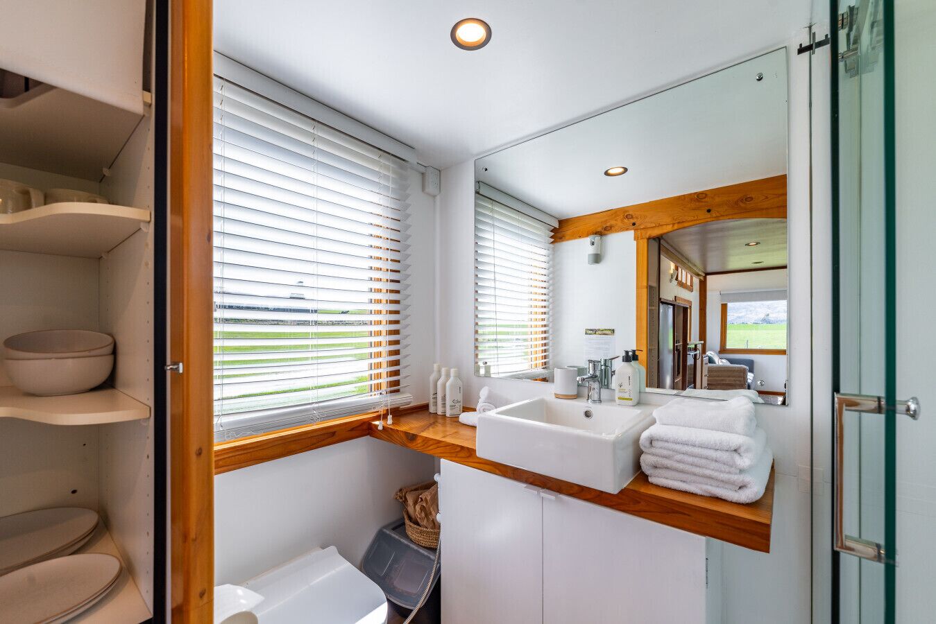 A bathroom with a wooden vanity, two sinks, a large mirror, and a view of the outdoors.