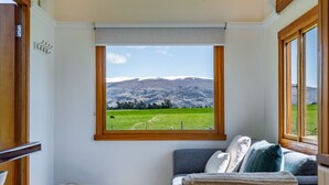 A cozy room with a large window offering a view of a green field and mountains.