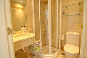 Een badkamer met een douche met glazen wand, een toilet, een wastafel met zeepdispensers en een glazen plank met toiletartikelen.