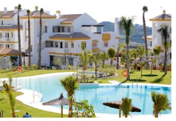 A resort with a large pool, palm trees, and white buildings with yellow accents. - CT 108 - Calanova (Mijas)