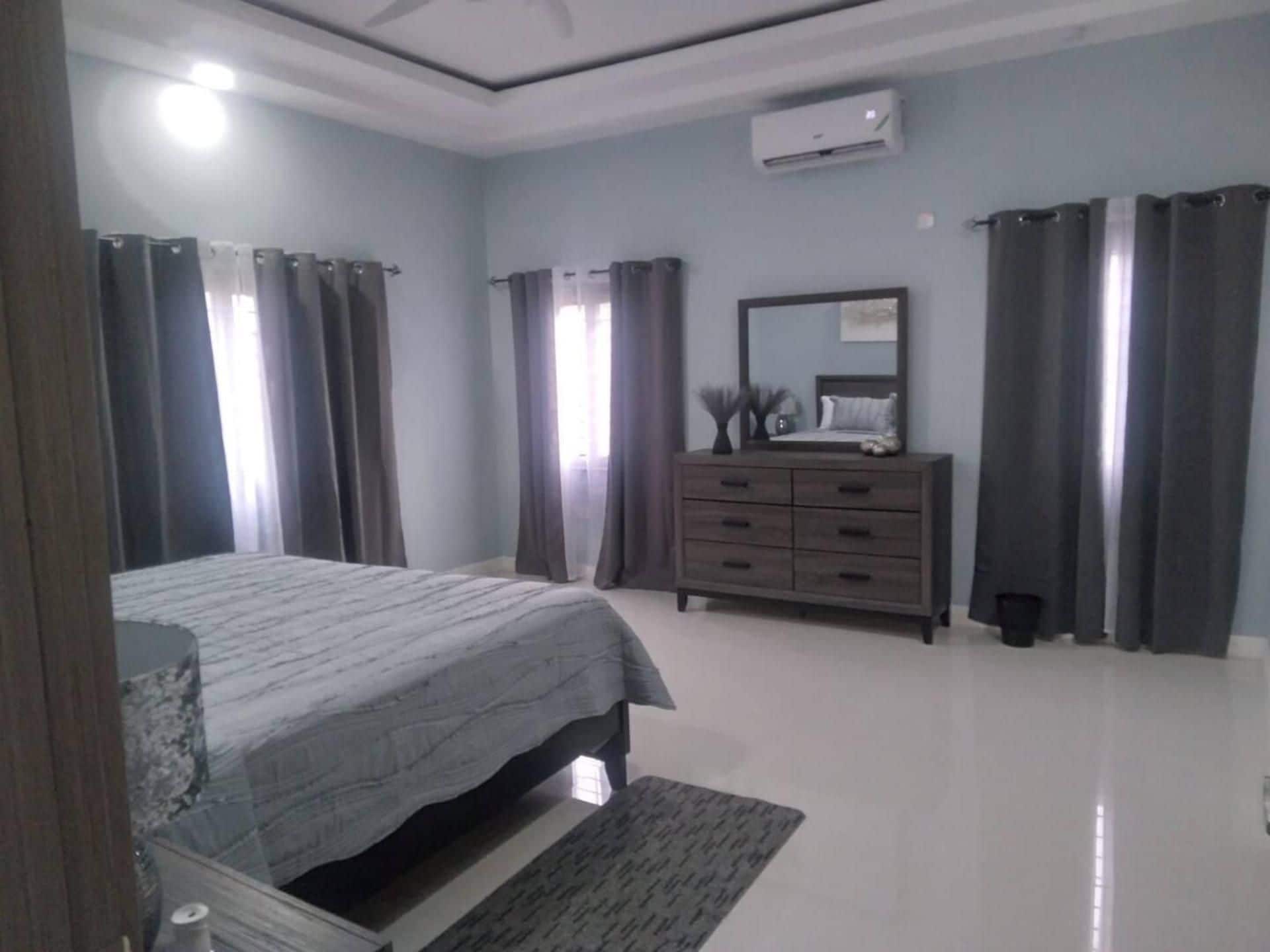 A bedroom with a bed, a dresser, a mirror, and curtains.