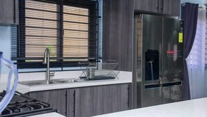 Una cocina moderna con un refrigerador de acero inoxidable, un lavamanos con grifo y una ventana con persianas.