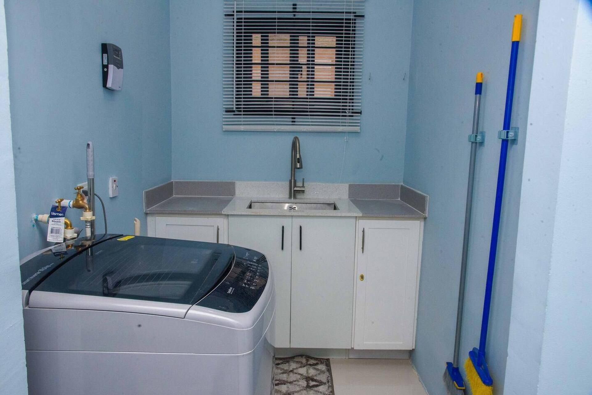 Una cocina compacta con lavadora, un lavamanos y una ventana con persianas.