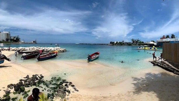 Una playa con barcos, agua cristalina y un litoral rocoso.