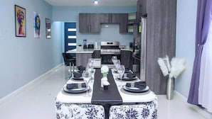 Un comedor con una mesa preparada para cuatro, una cocina al fondo y una pared azul con obras de arte.